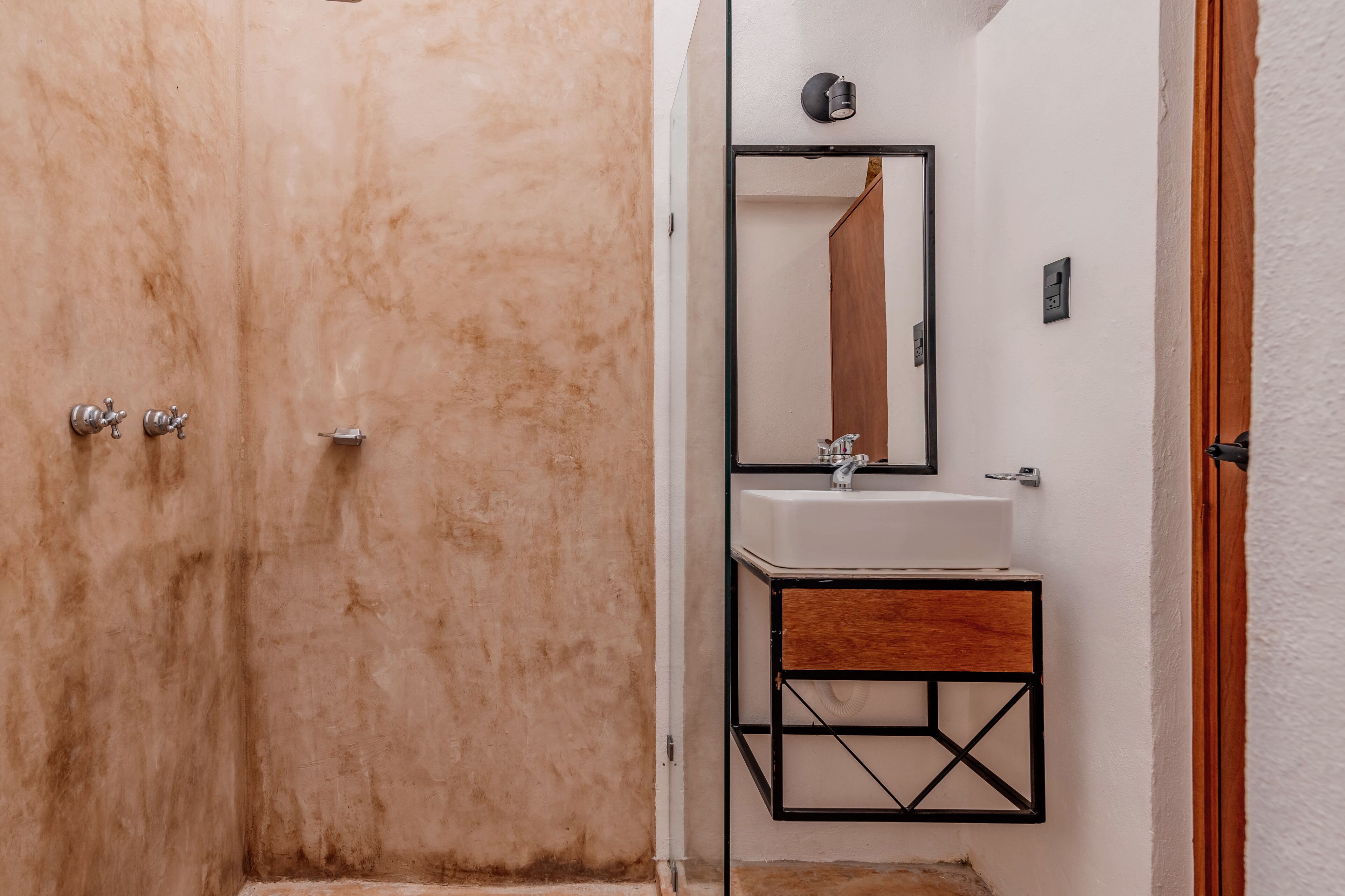 A bathroom with a marble shower, a white sink, and a wooden vanity.