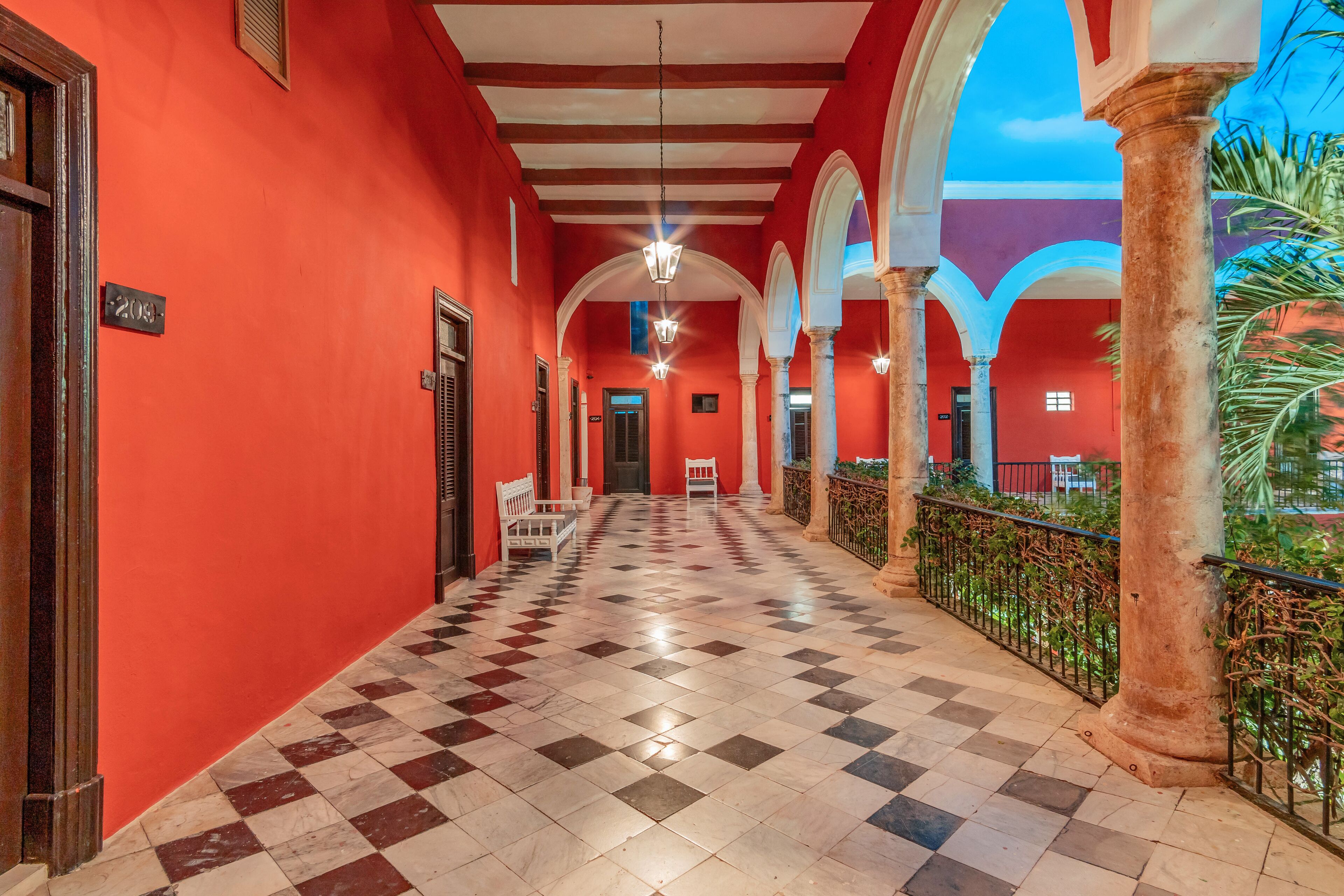 A corridor with red walls, checkered flooring, and white benches.