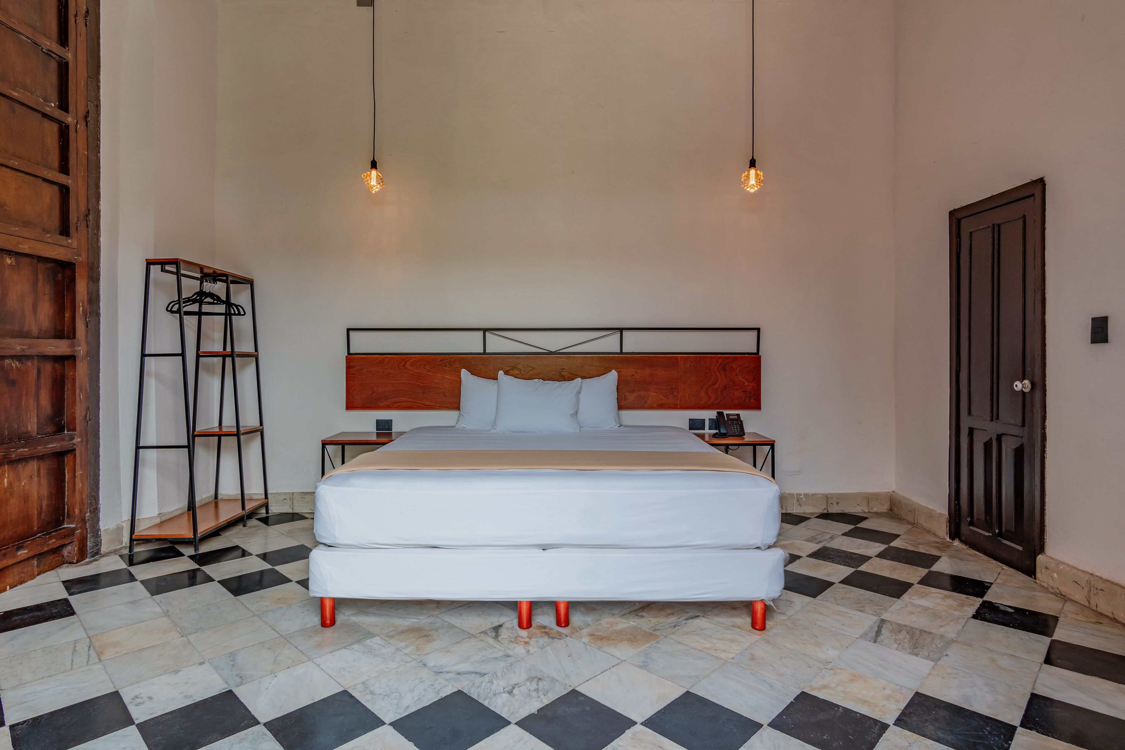 A double bed with a wooden headboard, two bedside tables, and a hanging light fixture.