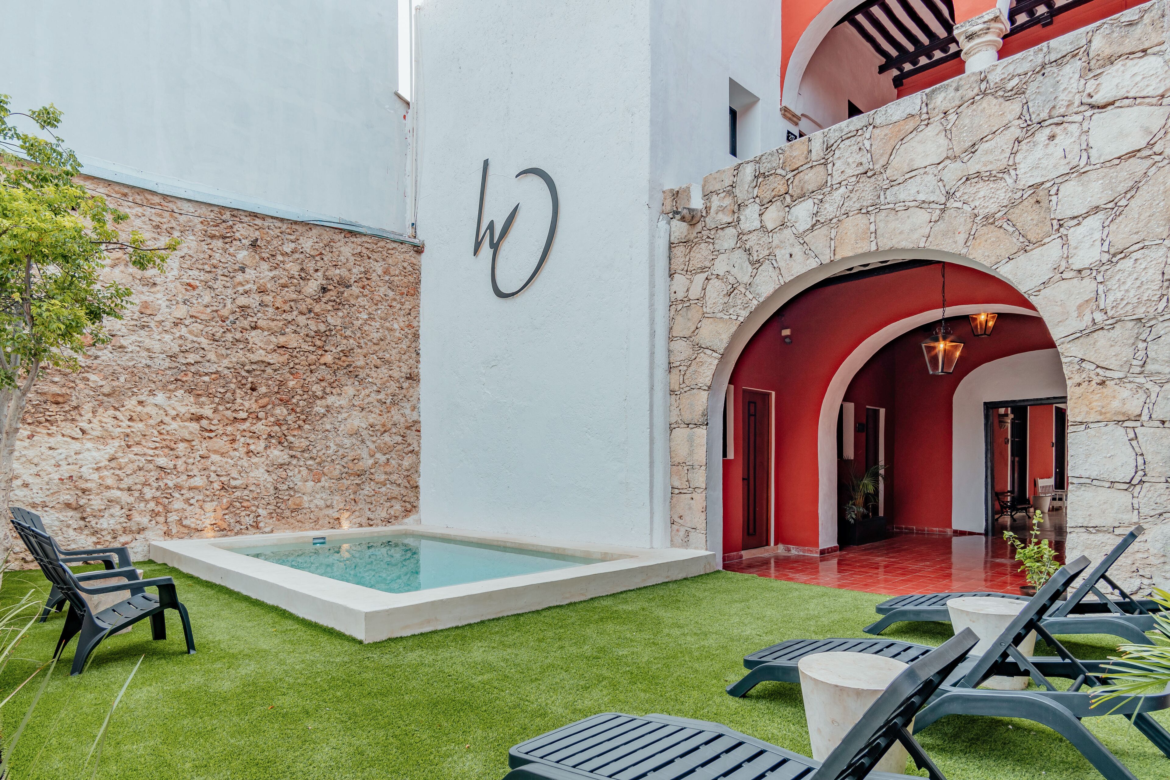 A pool area with lounge chairs, a stone wall, and a red archway leading to a covered patio.