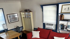 A living room with a red sofa, a wooden table, a patterned rug, a bookshelf, and a radiator. - Waterfront Cottage on the C&D Canal! (Chesapeake City)