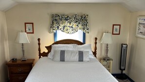 A neatly made bed with a wooden frame, two bedside tables with lamps, a wall-mounted radiator, and framed pictures on the walls. - Waterfront Cottage on the C&D Canal! (Chesapeake City)