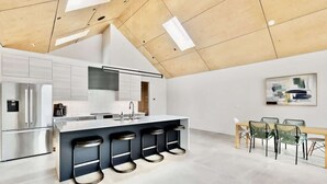 A modern kitchen with a central island, bar stools, a dining area with a bench and chairs, and a ceiling with skylights.