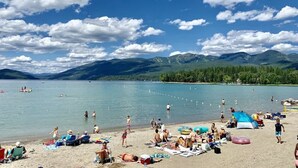 A beach with people, tents, and a lake with mountains in the background.