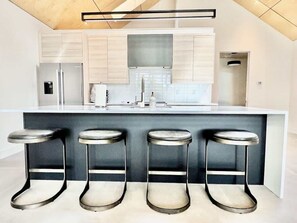 Cozinha moderna com ilha central, quatro banquetas, eletrodomésticos de aço inoxidável e design minimalista.
