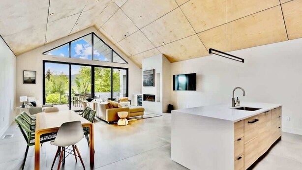 A modern kitchen with a large island, a dining area with a table and chairs, and a living space with a sofa and a TV.