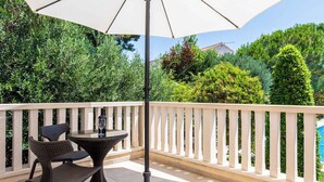 Eine Außenpatio mit Tisch und Stühlen unter einem großen Sonnenschirm, umgeben von einer weißen Balustrade und Grünpflanzen.