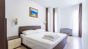 Ein Hotelzimmer mit Bett, Nachttisch, Lampe, einem Gemälde und einem Fenster mit Vorhängen.