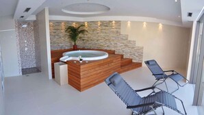 Un espace spa moderne avec un mur en pierre, un jacuzzi, des sièges en bois et une plante en pot.