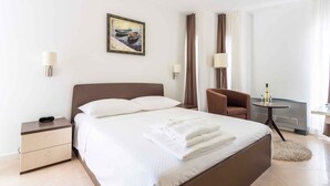 Een moderne hotelkamer met een groot bed, een nachtkastje, een stoel, een klein tafeltje met een lamp en een schilderij aan de muur.