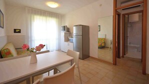 A compact living space with a dining area, kitchenette, and a bathroom visible through a glass door. - Holiday apartment with air conditioning and balcony (Bibione)
