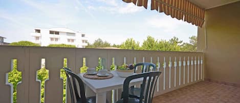 A balcony with a white table and chairs, a striped awning, and a view of a building and trees.