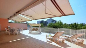 A covered outdoor area with a table and chairs, a swing, and a sun lounger. - Holiday apartment with air conditioning and roof terrace (Bibione)