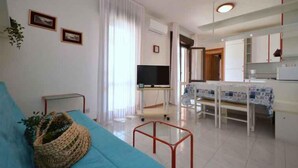 A modern living room with a sofa, a TV, and a kitchen area with a dining table and chairs. - Holiday apartment with air conditioning and roof terrace (Bibione)