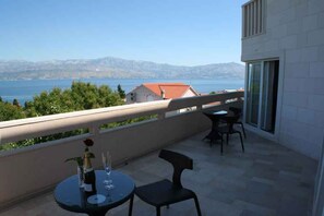 A balcony with a table and chairs, overlooking a body of water and mountains.