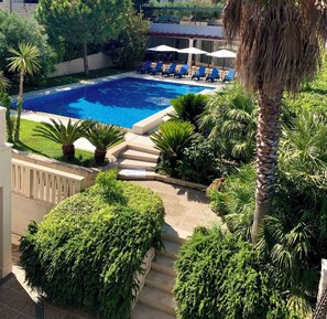 Uma piscina com espreguiçadeiras e guarda-sóis, cercada por vegetação exuberante e palmeiras.