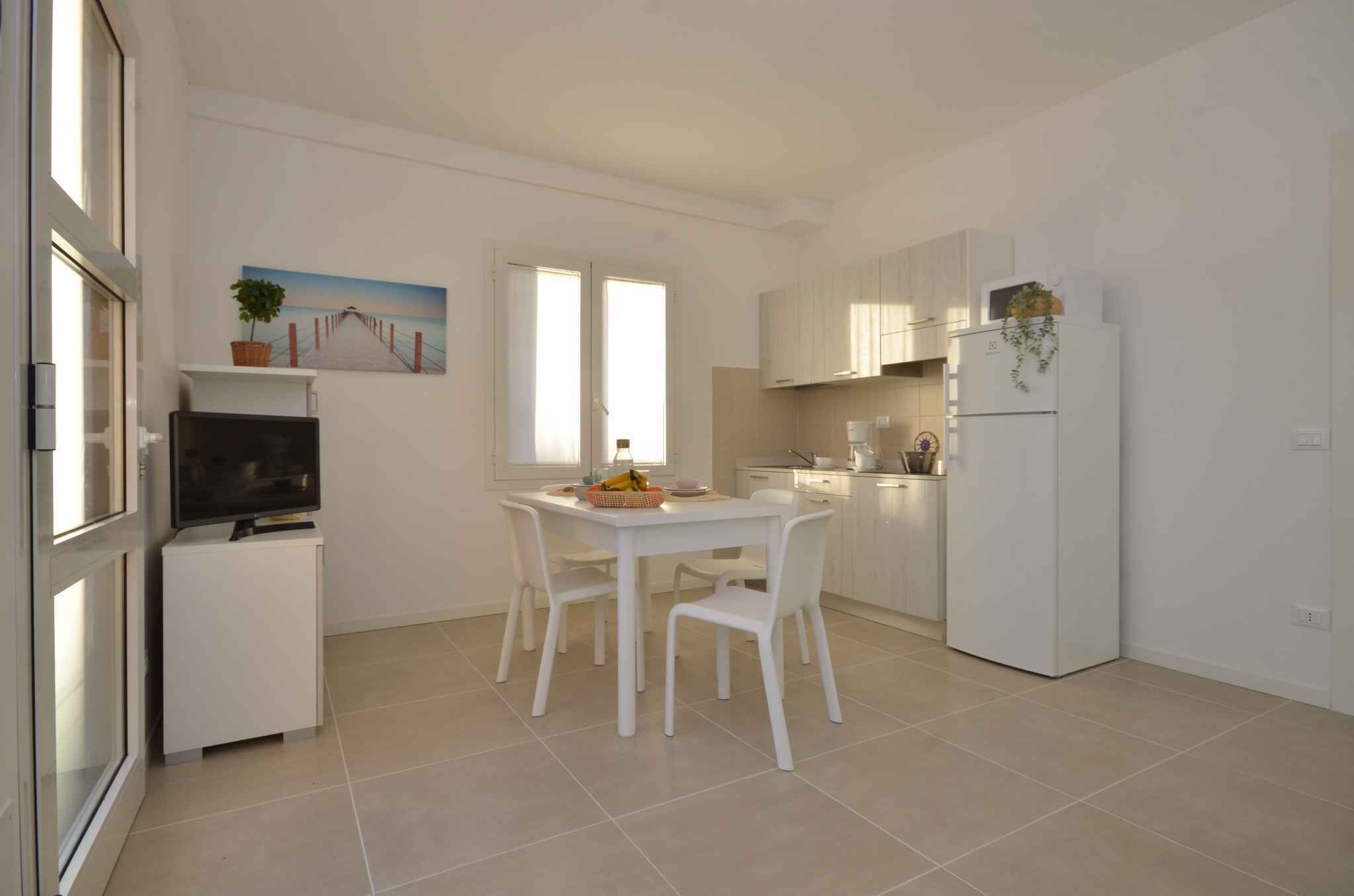 A modern kitchen with white cabinets, a dining table with chairs, a refrigerator, and a television on a stand.
