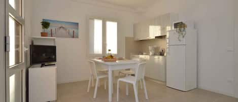 A modern kitchen with white cabinets, a dining table with chairs, a refrigerator, and a television on a stand.