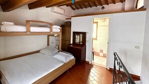Una stanza con soffitto in legno, un letto a castello, una scrivania con uno specchio e una porta che dà su un'altra stanza.