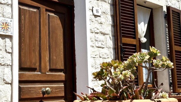 Un edificio con una porta in legno, una finestra con persiane e una pianta in vaso.