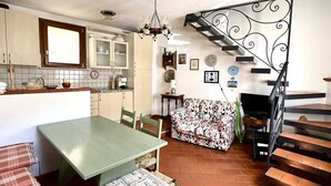 Una cucina con tavolo e sedie, un divano, una scala e un lampadario.