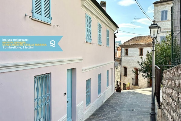 A narrow street with pastel-colored buildings, a stone wall, and a street lamp.