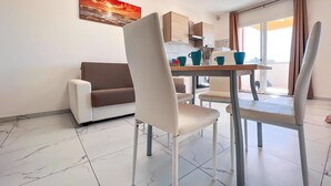 A modern living room with a sofa, dining table, chairs, and a kitchen area.
