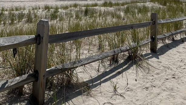 Ein Strand mit einer Holzlattenzaun, Sanddünen und dem Meer.