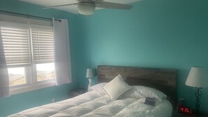 Ein Schlafzimmer mit einem Bett, einem Deckenventilator, einem Nachttisch mit Lampe und einer digitalen Uhr, die die Uhrzeit anzeigt.