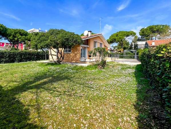 Une maison avec un toit en pente, une antenne parabolique et un petit jardin avec de la pelouse et des fleurs.