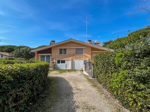 Une maison à deux étages avec une allée en gravier, un garage et une haie bien entretenue.