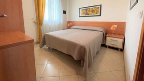 Ein Hotelzimmer mit Bett, Nachttisch, Lampe, einem Gemälde an der Wand und einem Fenster mit Vorhängen.