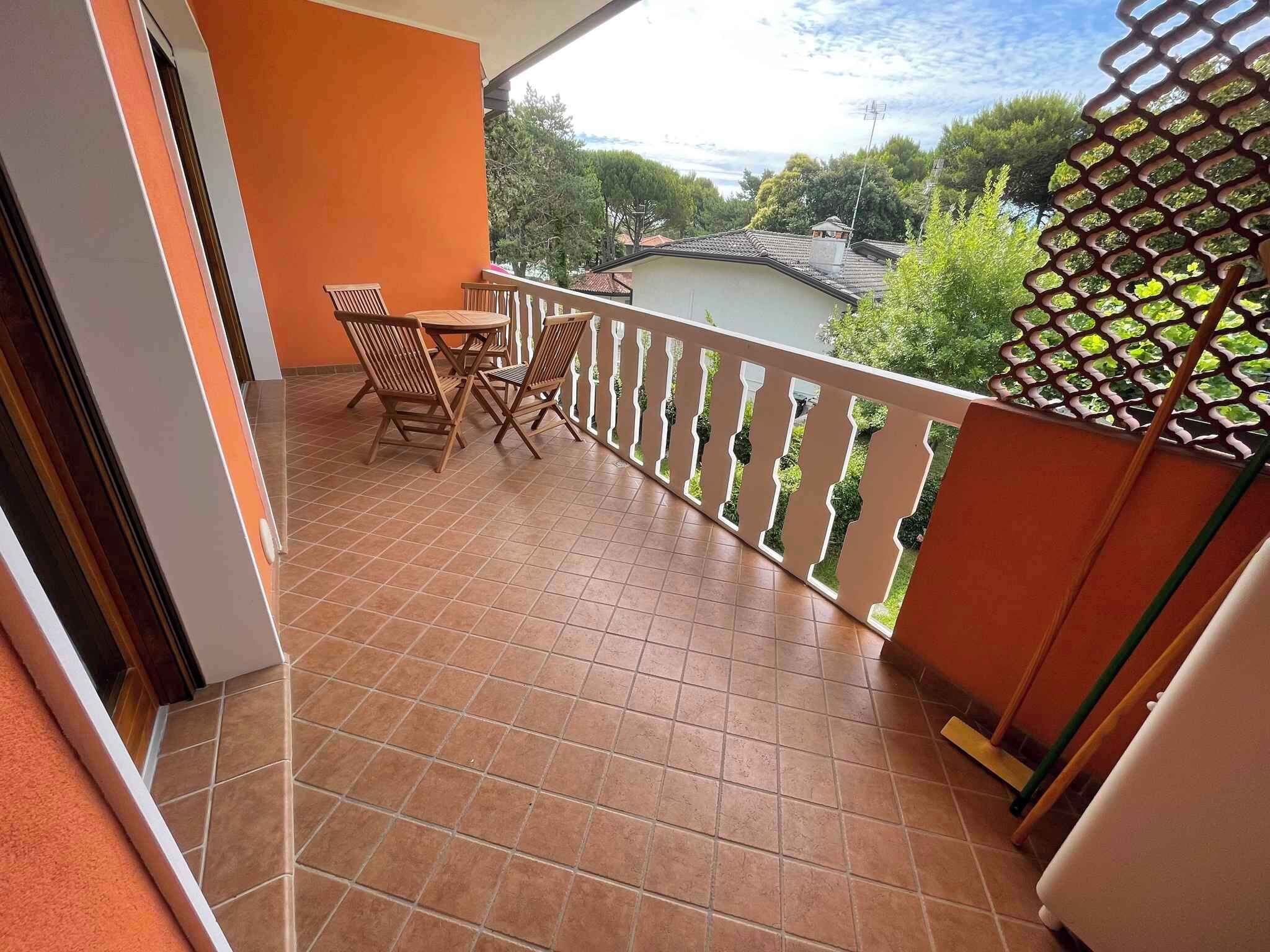 A balcony with a tiled floor, a table with chairs, and a view of greenery and buildings in the distance.