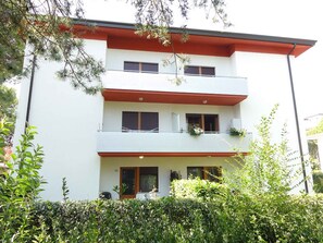 Ein mehrgeschossiges Gebäude mit Balkonen, einem überdachten Eingangsbereich und einem gepflegten Garten.