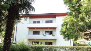 A multi-story building with a white facade and red roof, surrounded by well-maintained greenery and a clear pathway leading to the entrance. - Holiday apartment in a quiet and central location, completely renovated (Bibione)