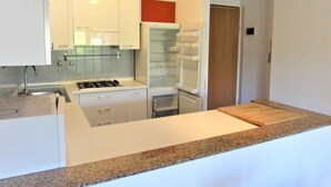 A modern kitchen with white cabinets, a granite countertop, a built-in oven, and a refrigerator. - Holiday apartment in a quiet and central location, completely renovated (Bibione)