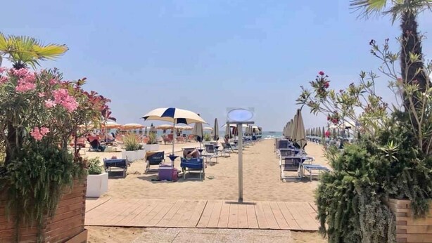 A beachside walkway leading to a row of beach chairs and umbrellas, with a clear view of the sea in the background.