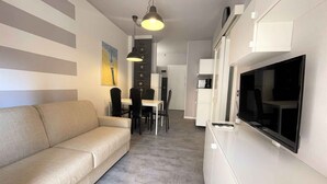 A modern living room with a sofa, dining table, chairs, and a TV.