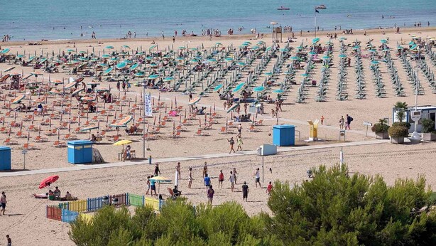 A beach with rows of sunbeds and umbrellas, a lifeguard tower, and a clear view of the sea.