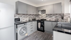 A modern kitchen with grey cabinets, a built-in oven, microwave, and washing machine.