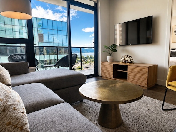 A modern living room with a sofa, a round coffee table, a TV, and a balcony with a view of a building and the sky.