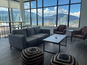 A modern living room with a sofa, two armchairs, a coffee table, and a view of a lake and mountains.