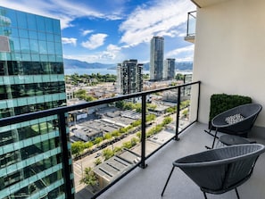 A balcony with two chairs, a view of a cityscape, and a building with reflective glass windows.