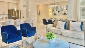 A modern living room with a sofa, two blue armchairs, a coffee table, and a ceiling fan. - Beautiful 4BD/3BA Townhome with Pool 280 (Kissimmee)