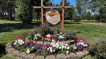 A welcome sign for Sandtrap Golf Course in Lakeville, MN, surrounded by a flower bed with various flowers.