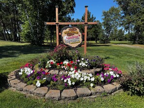Welkomstbord voor Sandtrap Golf Course in Lakeville, MN, omgeven door een bloembed met diverse bloemen.