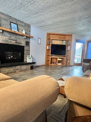 A living room with a fireplace, a television, and a bookshelf. - Large Private Condo on the Golf Course close to Many Lakes! (Cass Lake)
