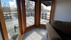 A corner room with a wooden floor, a brown sofa, and a view of an outdoor deck with a picnic table. - Large Private Condo on the Golf Course close to Many Lakes! (Cass Lake)