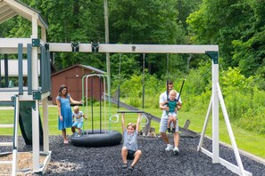A playground with swings and a slide, surrounded by greenery.