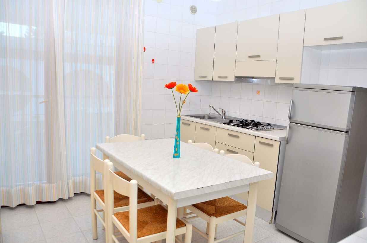 Een keuken met witte kasten, een roestvrijstalen koelkast en een eettafel met stoelen.